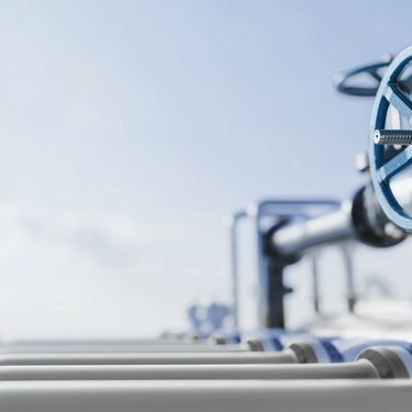 heller Himmel, graue Gasrohre und ein blaues Ventilrad